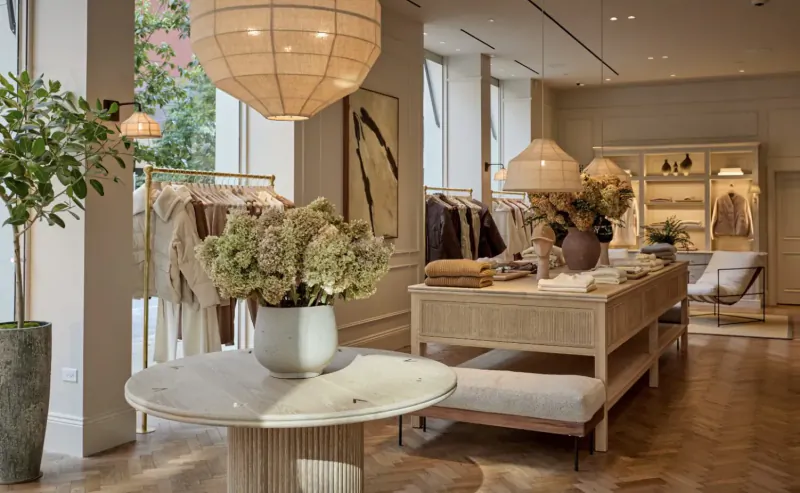 Varley SoHo flagship store interior: racks of neutral clothing, hydrangeas, rattan table, pendant lamps, wood floors.