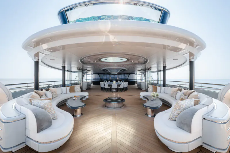 Luxury yacht Kismet's expansive white deck with curved sofas, central table, bar, and ocean view