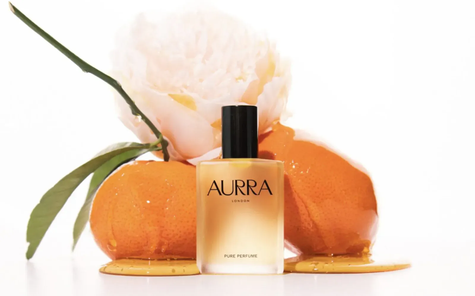 AURRA Pure Neroli luxury perfume bottle with oranges, peony flower, and leaves on white surface