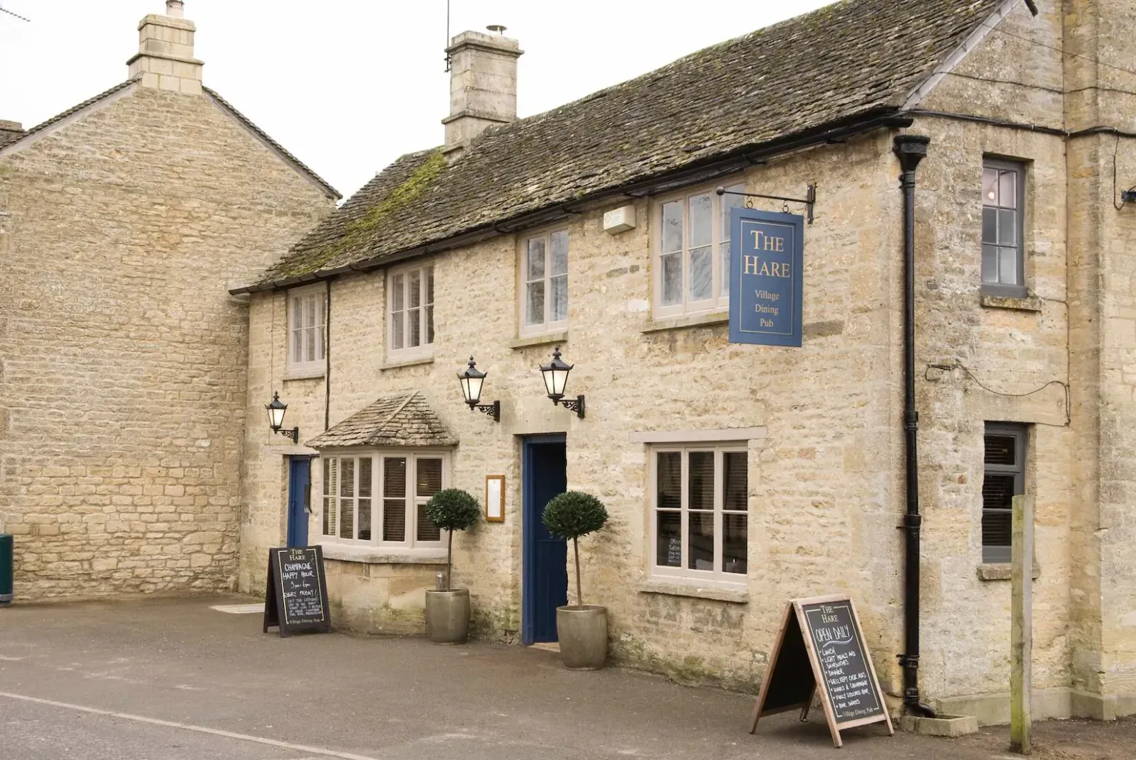 The Fox Inn pub, a stone Cotswold building with blue sign, lanterns, plants, and chalkboard easel outside.