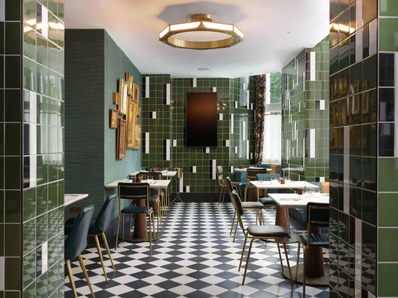 Elegant green-tiled dining room at The Other House with black-and-white checkered floor, round ceiling light, and empty tables and chairs.