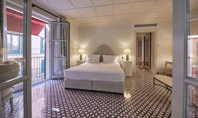 Elegant Hotel Cappuccino bedroom with white bed, lamps, patterned tile floor, and open balcony doors to Palma view.