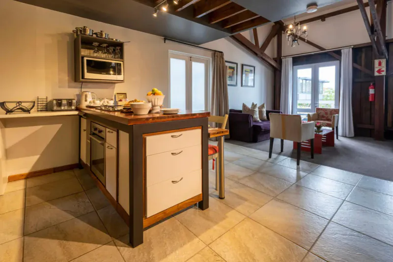 Modern loft kitchen at The Lofts Boutique Hotel with wooden beams, island counter, fruit bowl, and lounge seating.