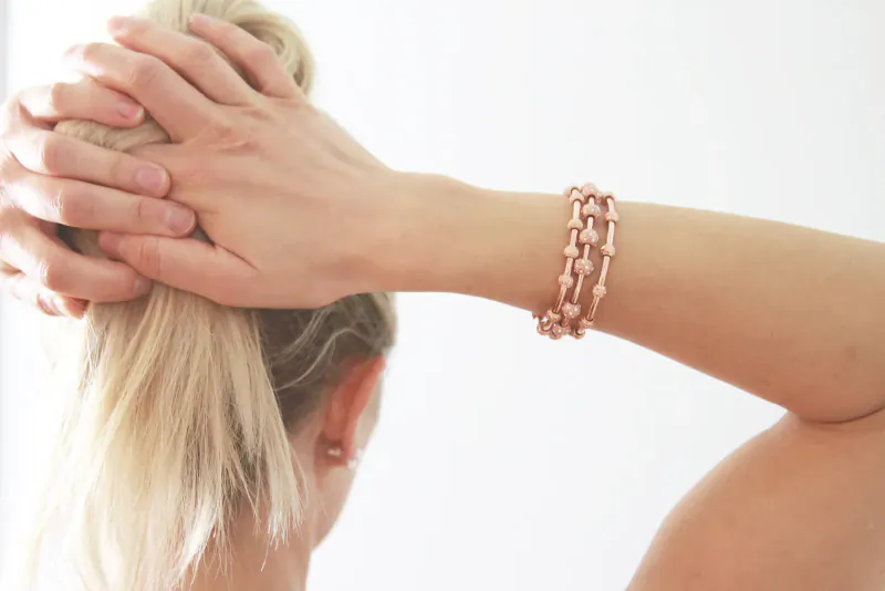 Close-up of woman's hand holding blonde ponytail, showcasing rose gold chain-link bracelet on wrist