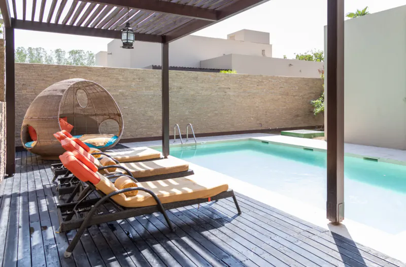 Luxury pool deck at Melia Desert Palm Dubai with orange loungers, egg chair under pergola, and turquoise pool.