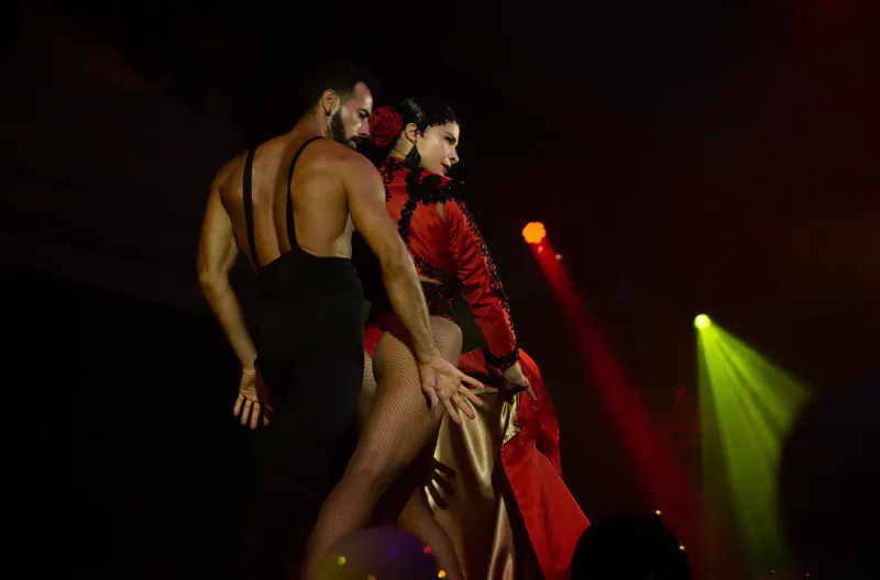 Passionate tango dancers in red and black attire perform intimately on Lio Cabaret Ibiza stage with red and green spotlights.