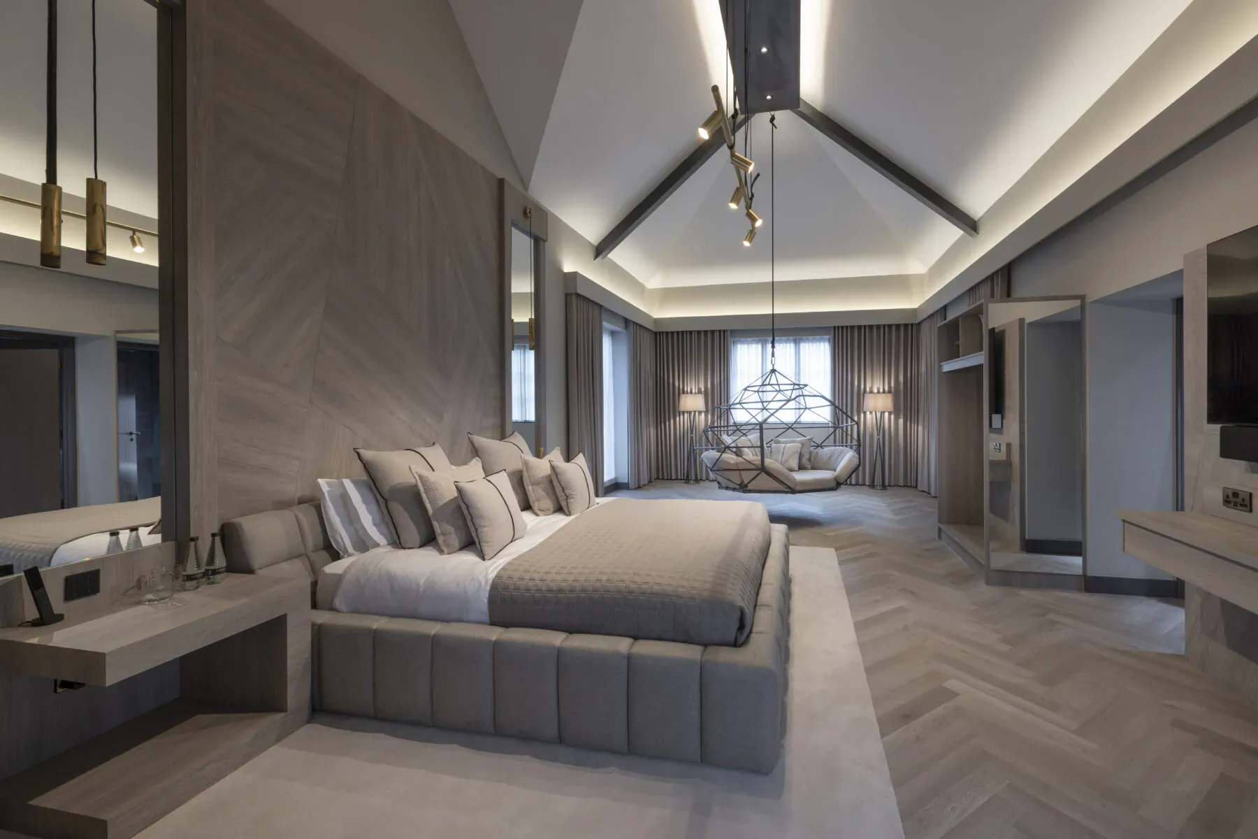Luxurious modern bedroom with tufted gray bed, herringbone floors, pendant lights, and large windows