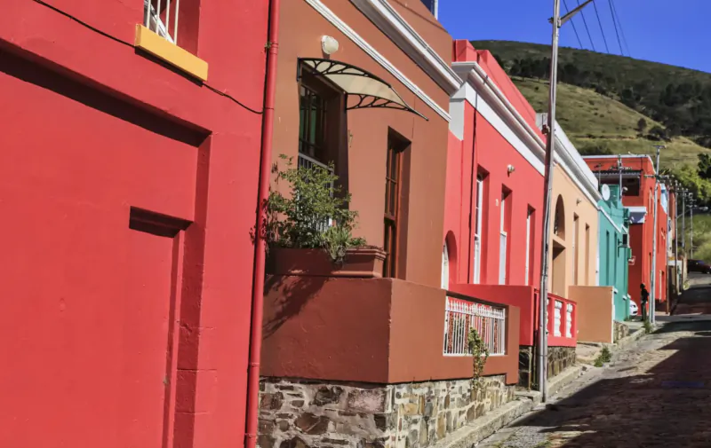 Colorful row of Bo-Kaap houses in vibrant reds, oranges, teal on steep cobbled street with hills behind