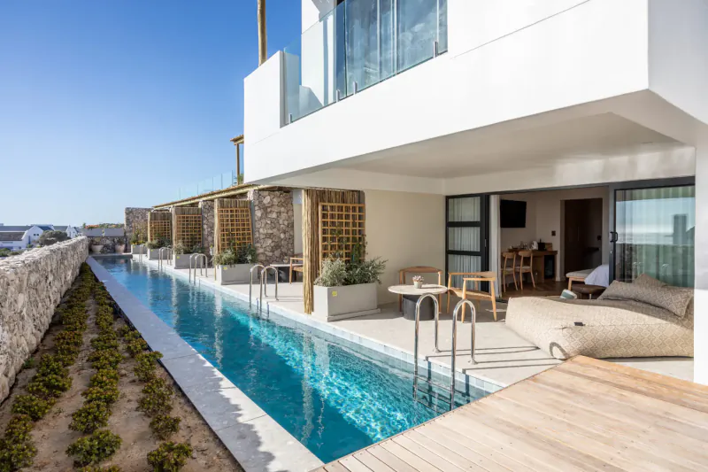 Infinity pool beside modern white Oyster Suites at Abalone Hotel & Villas, with lounge furniture and ocean views.