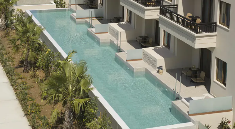 Aerial view of infinity pool at Asterion Suites & Spa, Crete, with white modern villas, palm trees, and lounge chairs.