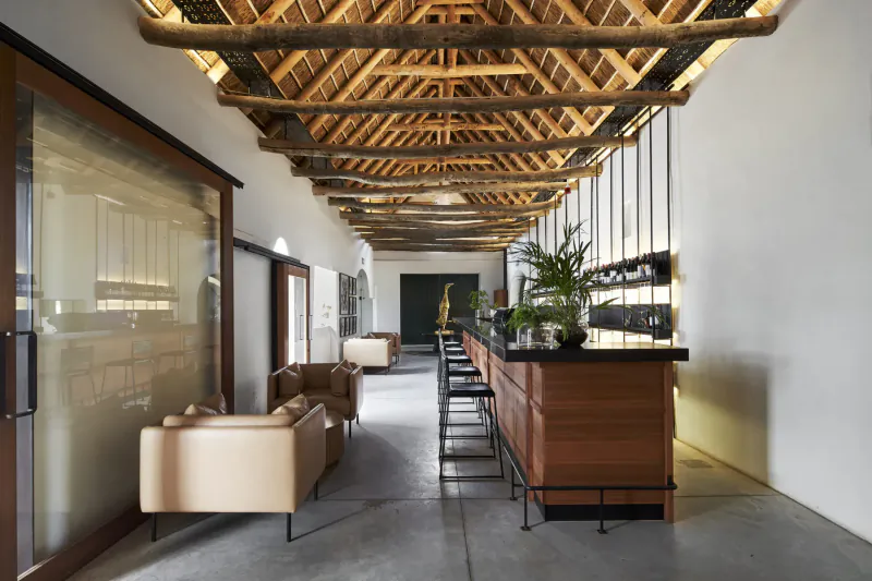 Clara’s Barn at Vergenoegd Löw: spacious gallery with wooden beamed ceiling, wooden bar, plants, and beige sofas.