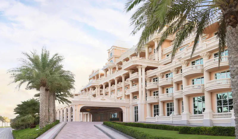 Raffles The Palm Dubai luxury hotel exterior with palm trees, pink pathway, and manicured gardens at dusk.