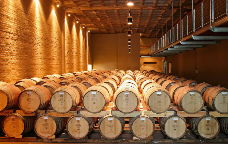 Rows of wooden wine barrels stacked in a warmly lit brick winery cellar at Groot Constantia