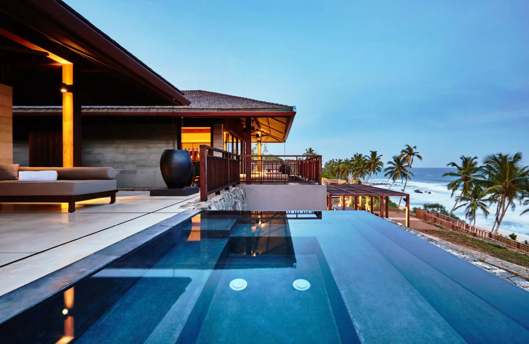 Infinity pool on balcony of Ani Private Resort villa at dusk, overlooking beach and palm trees.
