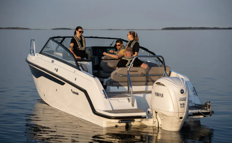 White Quarken 27 bowrider boat with Yamaha outboard on calm water, three people in leis seated aboard at boat show