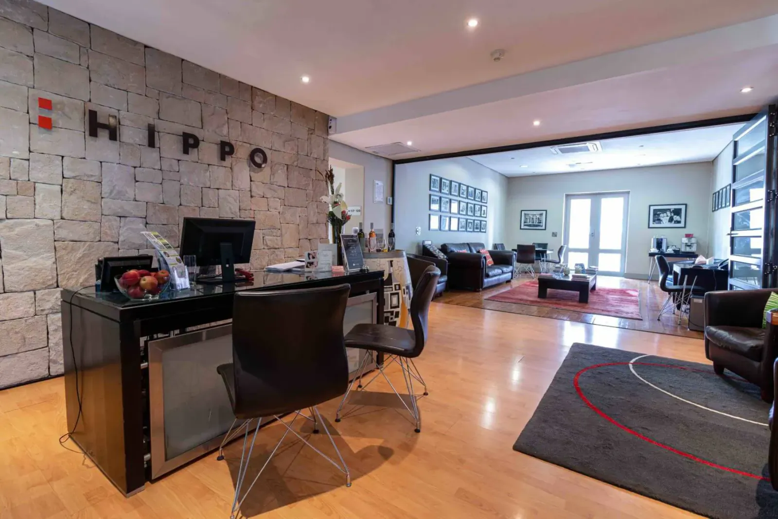 Hippo Boutique Hotel reception desk with 'HIPPO' logo on stone wall, apples, computer, and lounge area beyond.