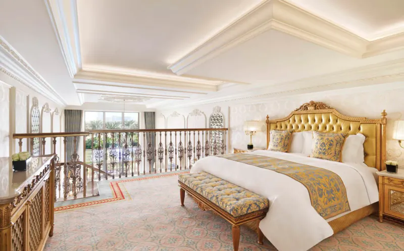 Luxurious Raffles The Palm Dubai suite with ornate gold king bed, balcony overlooking palms, elegant decor.