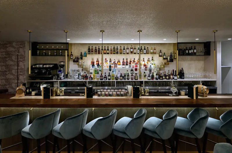 Elegant Kahani bar with backlit shelves of colorful liquor bottles, wooden counter, and blue velvet stools