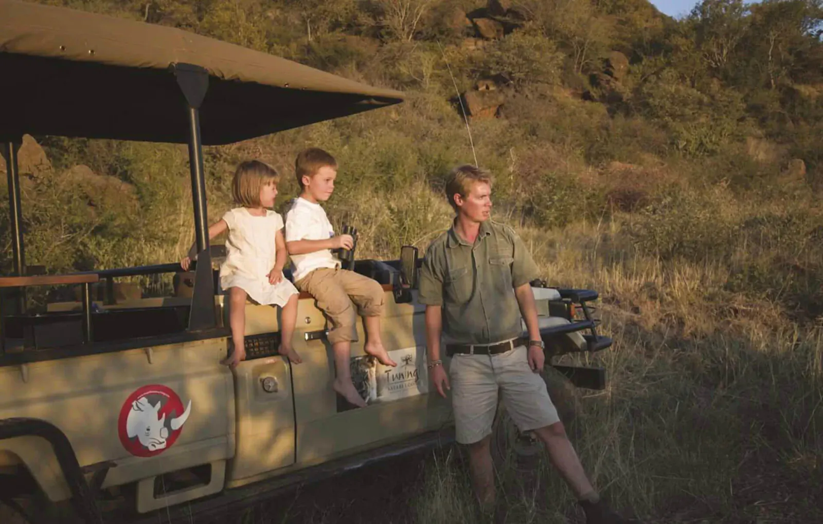 Family with young boy and girl sitting on safari jeep beside guide at Tuningi Safari Lodge, Madikwe Game Reserve