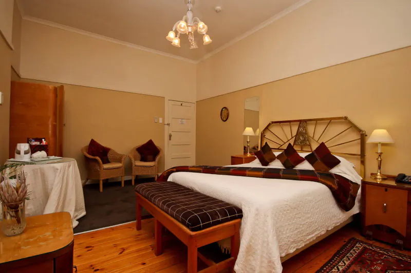 Elegant Montagu Country Hotel bedroom with king bed, plaid pillows, armchairs, lamps, and wooden floors.