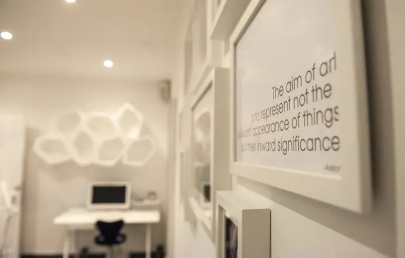 Modern clinic interior with framed quote: 'The aim of art is not the representation of things but the experience of their significance' amid white decor.