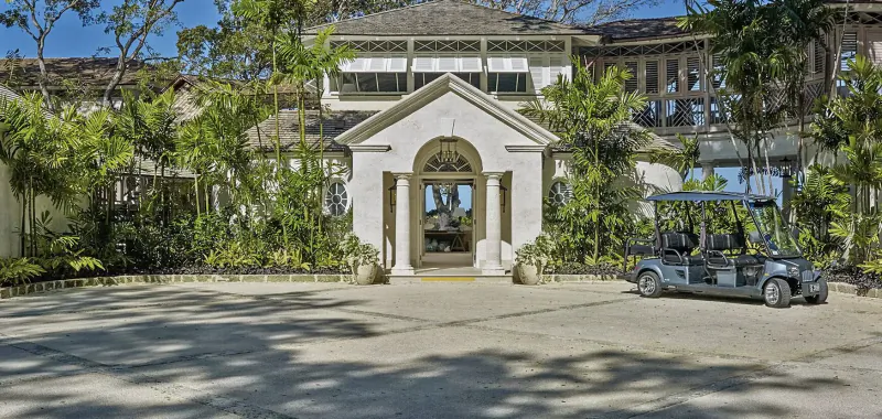 Luxury tropical villa entrance with arched white portico, palm trees, and parked golf cart on sunlit courtyard.