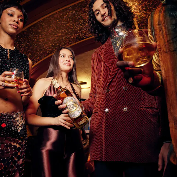 Diverse group in elegant club attire holding glasses and limited-edition Havana Club x Jonathan Raksha bottle.