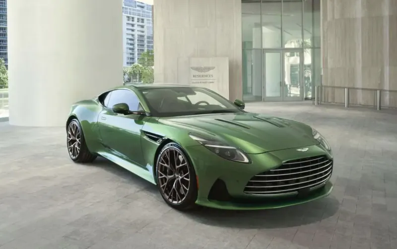 Emerald green Aston Martin DB11 sports car parked in modern lobby of Aston Martin Residences Miami with glass walls and high-rises outside.