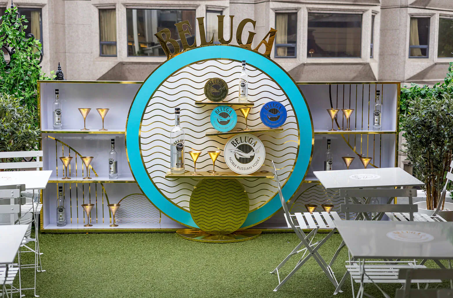 Beluga Vodka display with 'BELUGA' sign, blue wave backdrop, glassware on shelves, rooftop terrace with tables and plants