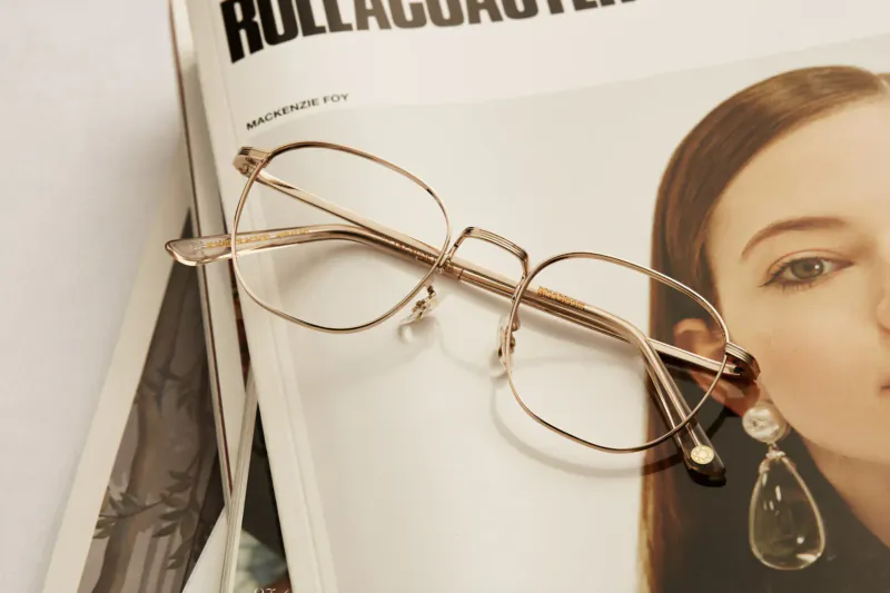Gold wireframe glasses resting on 'ROLLAGUST' magazine featuring a woman with drop earrings