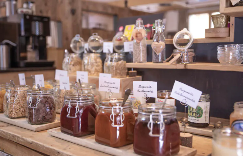 Wooden shelf in Hotel Kösslerhof displaying jars of nuts, grains, honey, and labeled bulk foods like muesli.