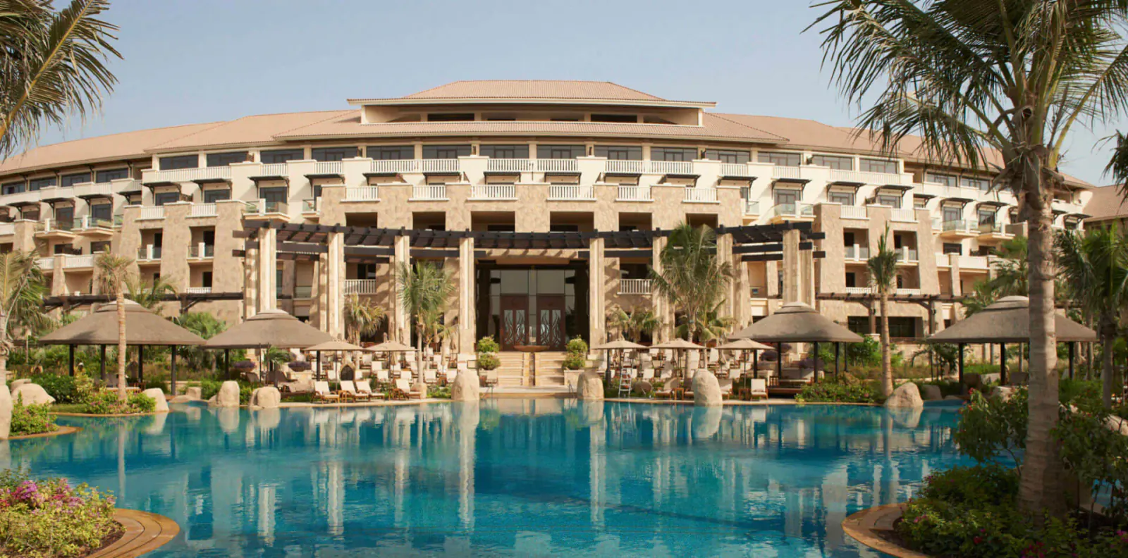Sofitel Dubai The Palm resort with beige arched facade, palm trees, lounge chairs, and blue pool in front.