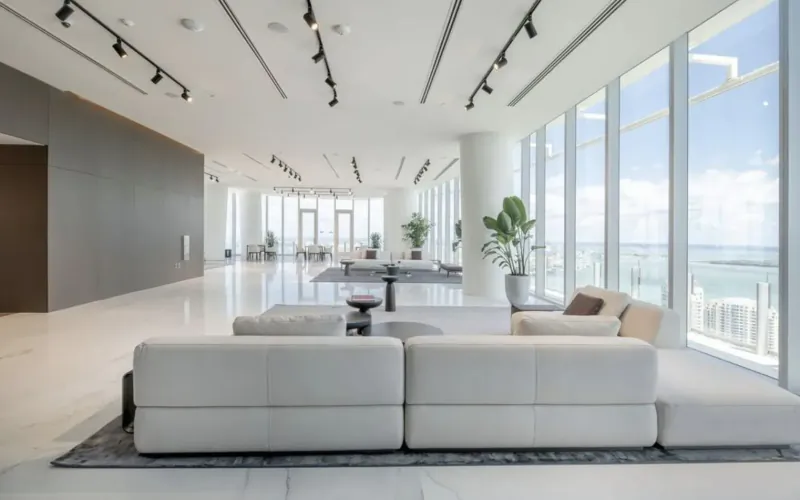 Spacious modern lobby of Aston Martin Residences Miami with white modular sofas, tables, plants, and ocean views through large windows.