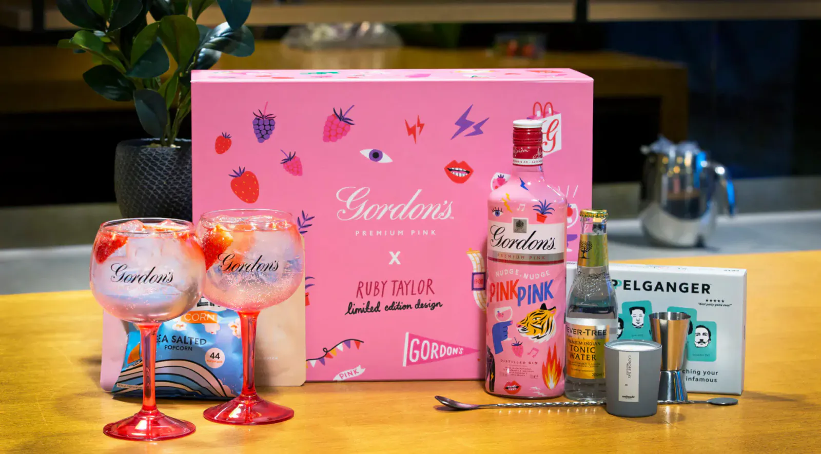 Pink Gordon’s gin gift set for Valentine’s: bottle, matching glasses, mixer, and accessories on table.