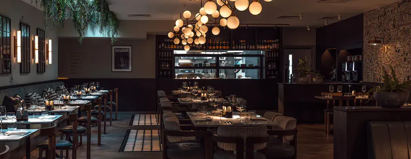 Elegant interior of Treadwell Restaurant in Oxford with wooden tables set for dining, pendant lights, open kitchen, and plants.