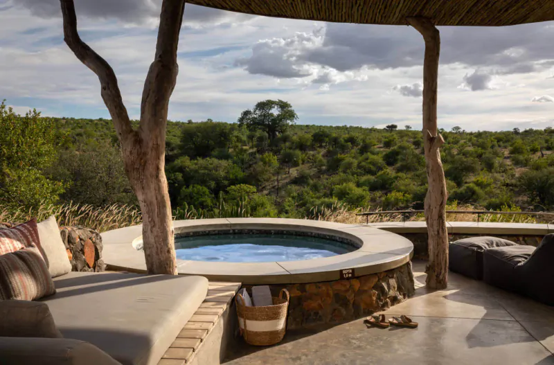 Outdoor hot tub with cushions on wooden deck under thatched roof, Mashatu bushveld landscape view