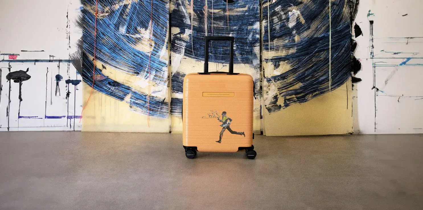 Orange Horizn Studios rolling suitcase with running figure sticker, before blue abstract wall art.
