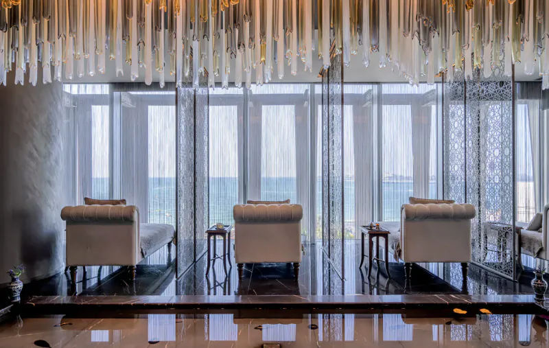 Elegant spa lounge at Naturelife Spa with white chaise lounges, crystal chandeliers, glass walls, and sea view