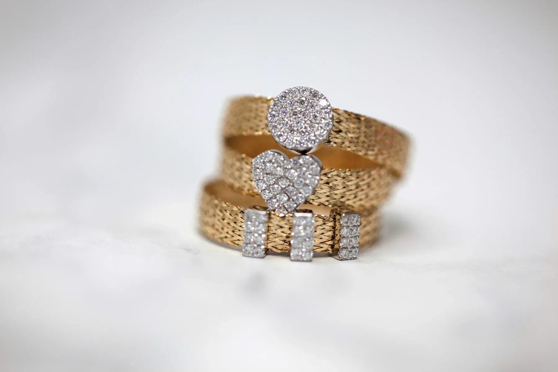 Stacked gold signet rings with diamond heart and round pavé accents on white background
