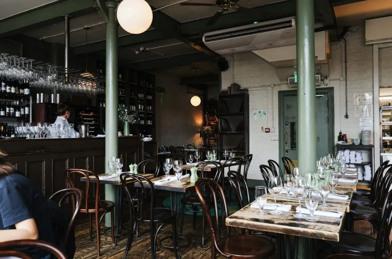 Elegant fine dining interior in Marylebone with wooden tables set for meals, bar, and globe lamps.