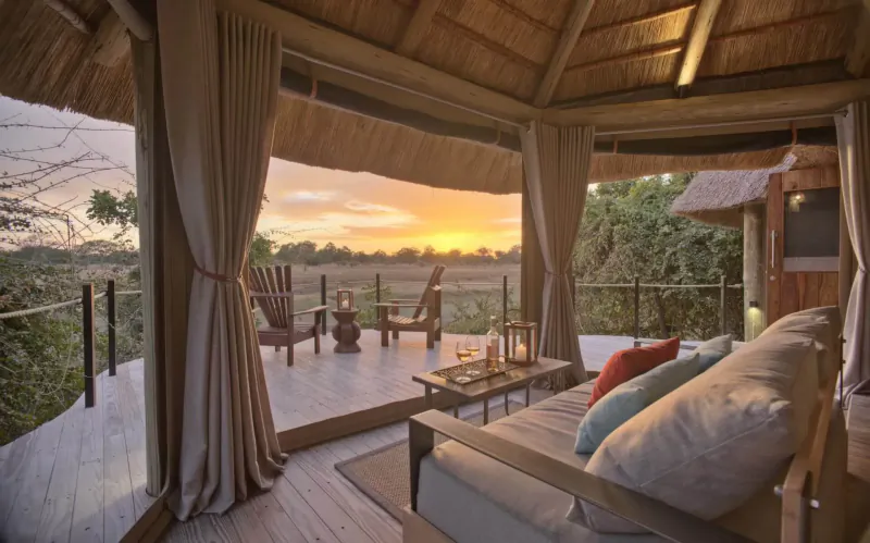 Luxurious Lion Camp tent interior with plush sofa, chairs, coffee table on deck overlooking savanna at sunset