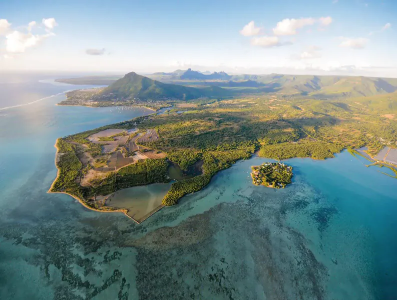 Aerial view of new Mauritian residential development on lush green peninsula with turquoise lagoons, beaches, and mountains.