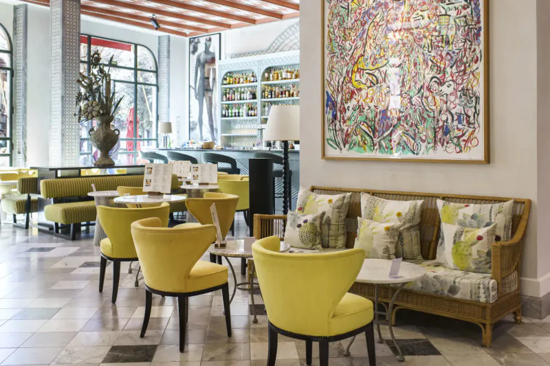Elegant Hotel Cappuccino lounge with yellow chairs, green cushions, abstract art, bar, and large windows.