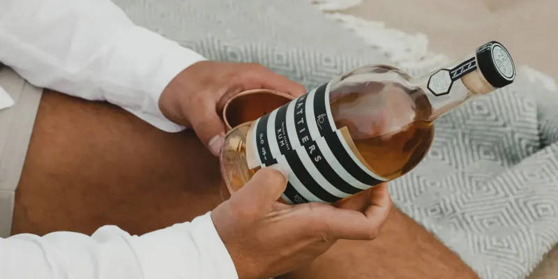 Man in white shirt holds striped 'Lillet' bottle and glass on beach blanket