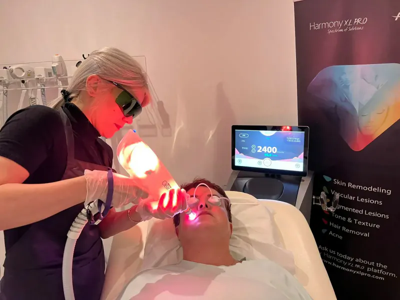 Woman therapist using Harmony XL laser on man's face in clinic, with 'Harmony XL', 'Skin Remodeling' banners.