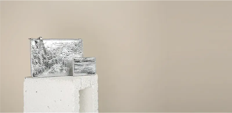 Silver textured Luxtra handbag and wallet displayed on white pedestal against beige background