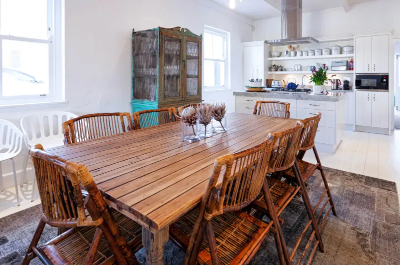 Spacious cottage kitchen with wooden dining table, rattan chairs, turquoise cabinet, and white cabinetry.