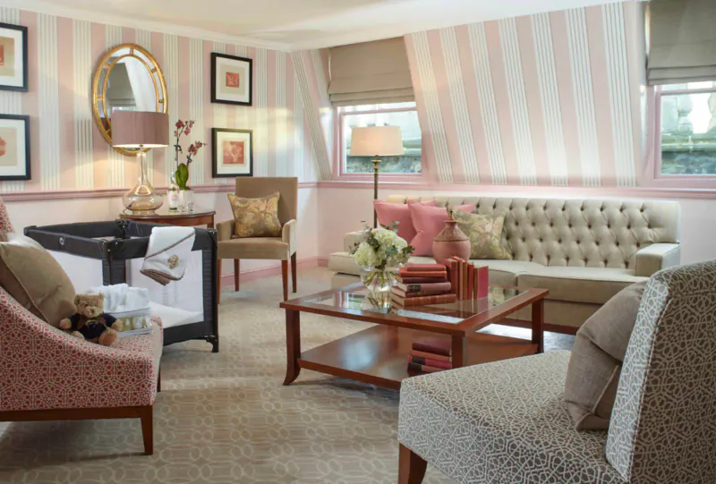 Elegant hotel living room at Royal Crescent Hotel & Spa with pink striped walls, tufted sofa, crib, flowers, and armchairs.