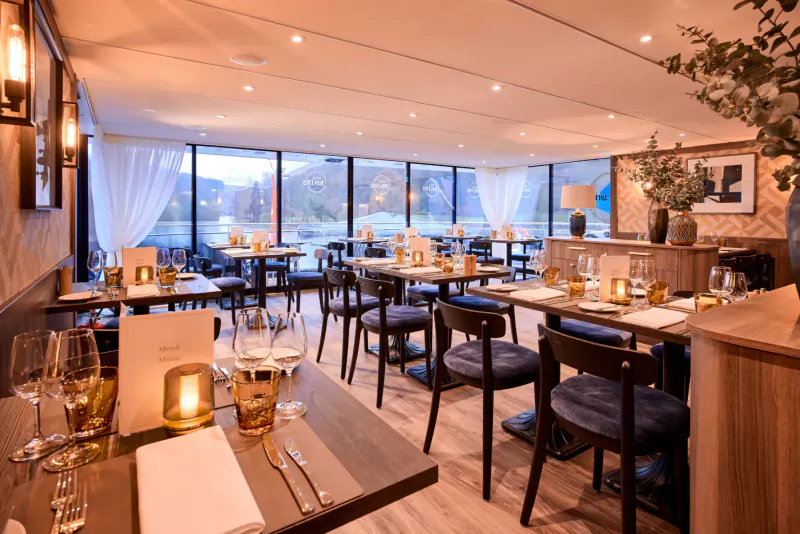 Elegant dining room on Viva Cruises ship with river views, warmly lit tables set with wine glasses and candles.