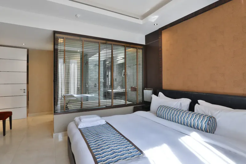 Luxurious hotel bedroom with king bed, blue pillows, folded towels, and glass-walled bathroom in Melia Desert Palm Dubai